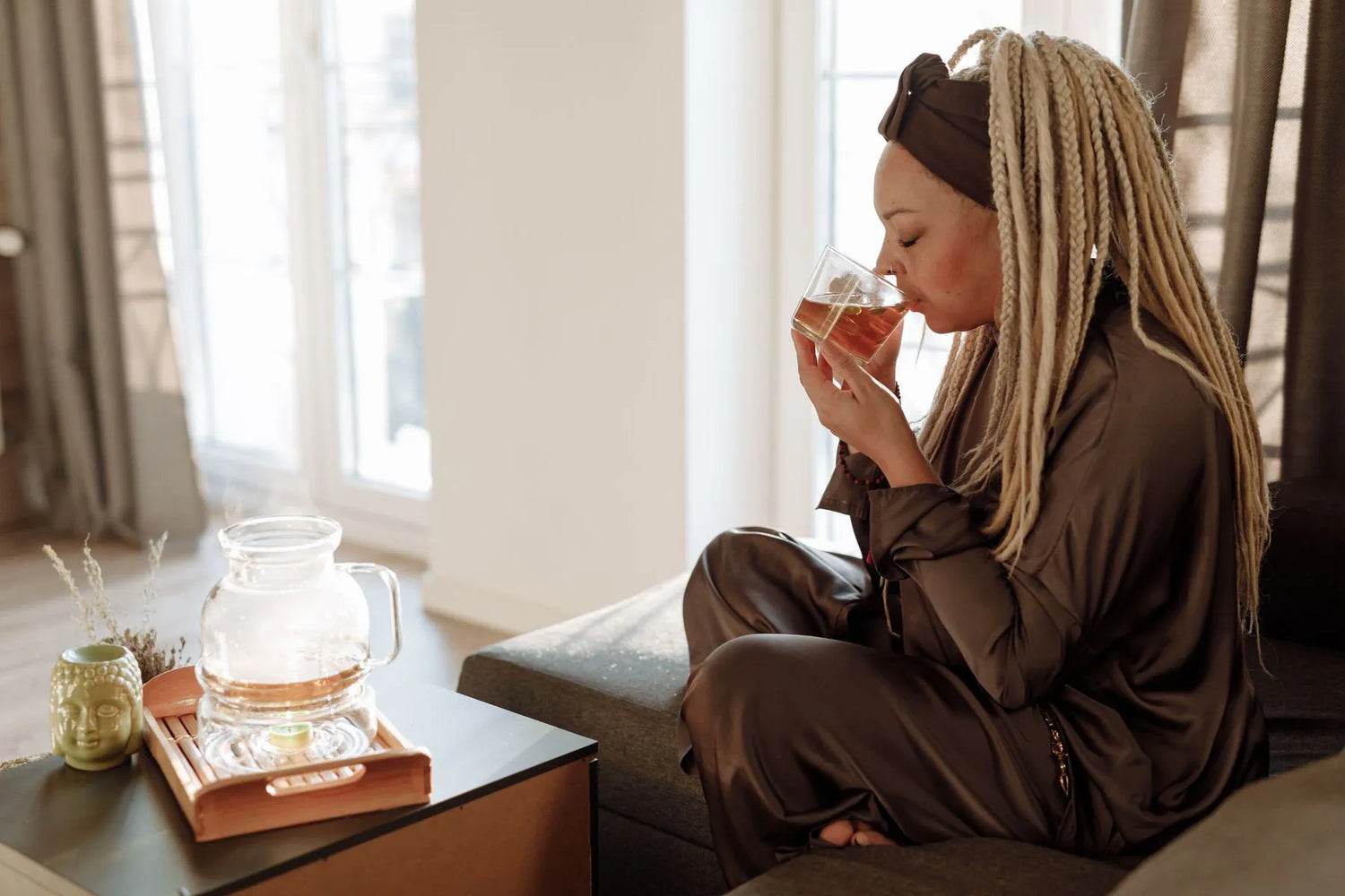 Woman in silk loungewear enjoying freshly brewed tea from a glass teapot